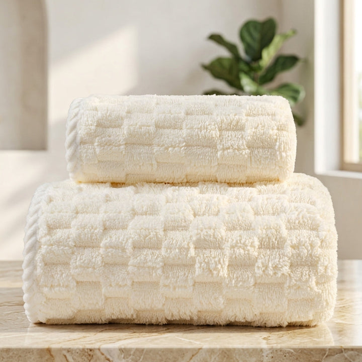Two rolled cream-colored fleece towels stacked on a marble surface.
