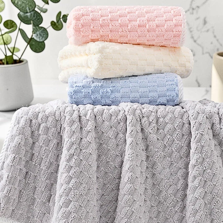 Stack of three soft fleece towels in pink, cream, and blue, with a larger grey towel in the foreground.