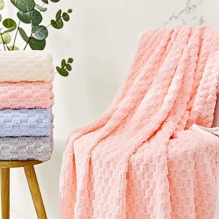Stack of four soft fleece towels in cream, pink, blue, and gray, with a pink fleece blanket draped over a chair.
