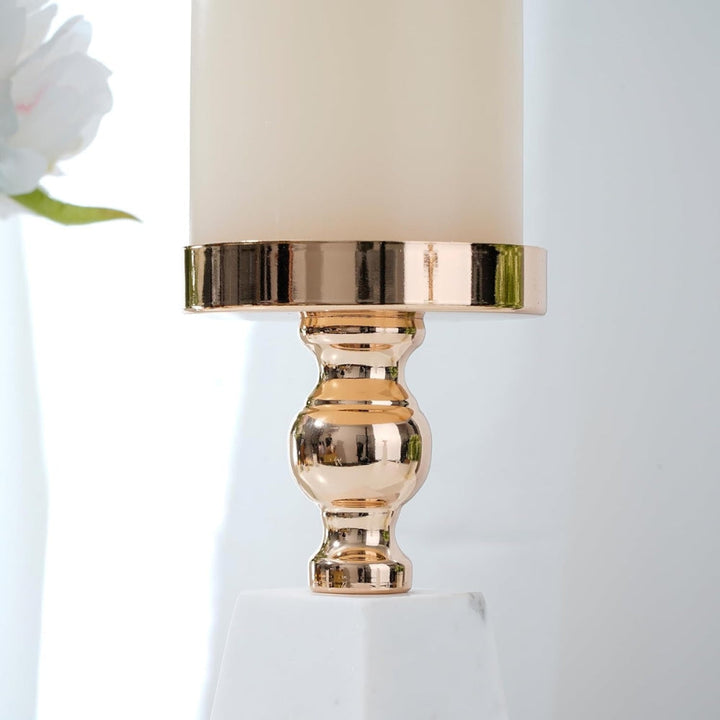 Gold metal candle holder with a cream candle on a marble base, with a white flower in the background.