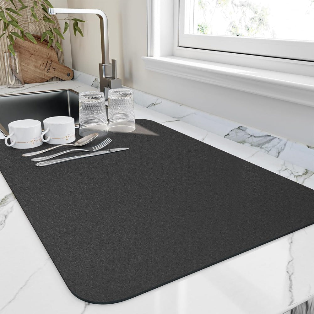 Dark grey diatomite quick-dry dish mat with two white mugs, two glasses, and cutlery on a marble countertop.