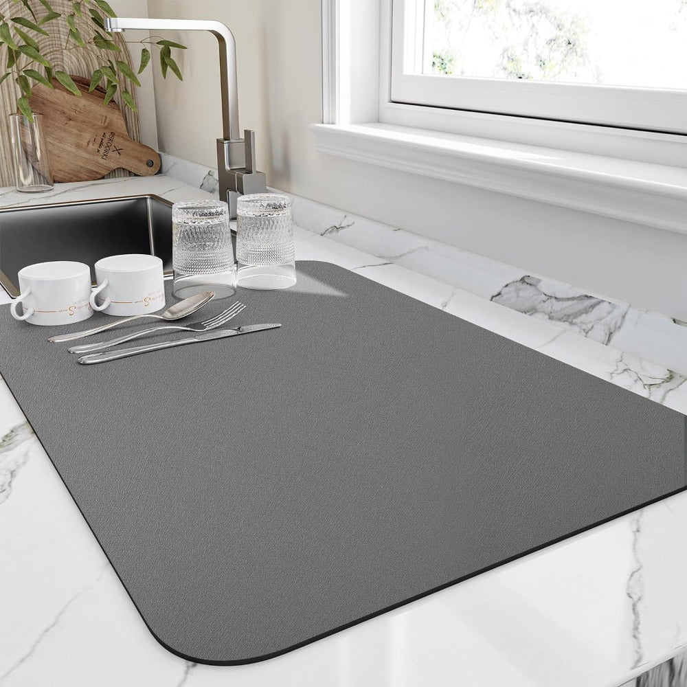 Gray diatomite dish mat on a marble countertop with cups, glasses, and cutlery.