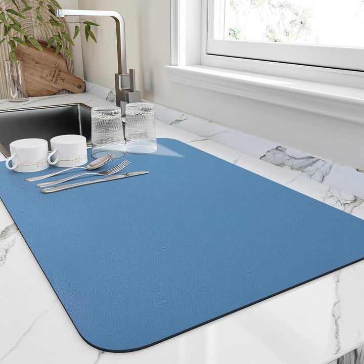 Blue diatomite dish mat with cups, glasses, and cutlery on a marble countertop.