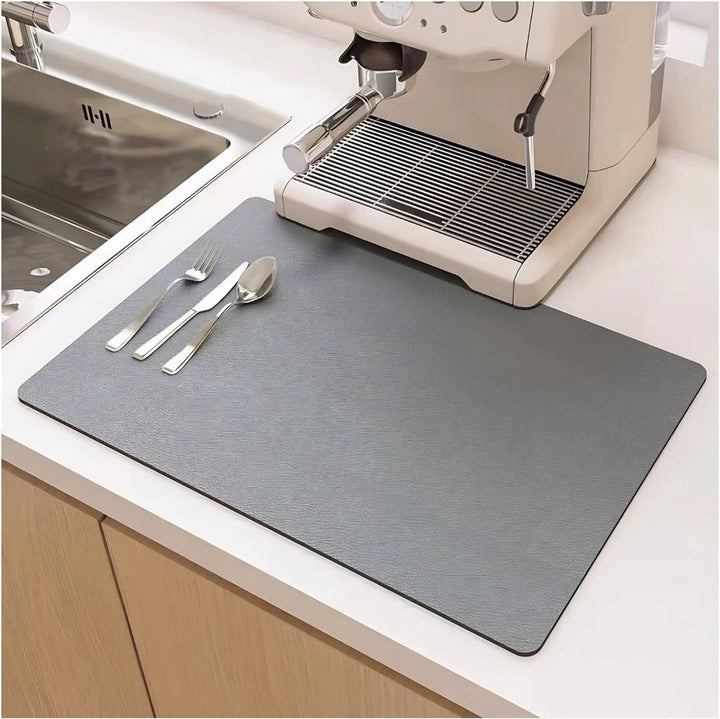 Gray diatomite quick-dry dish mat with cutlery and espresso machine on a kitchen counter.