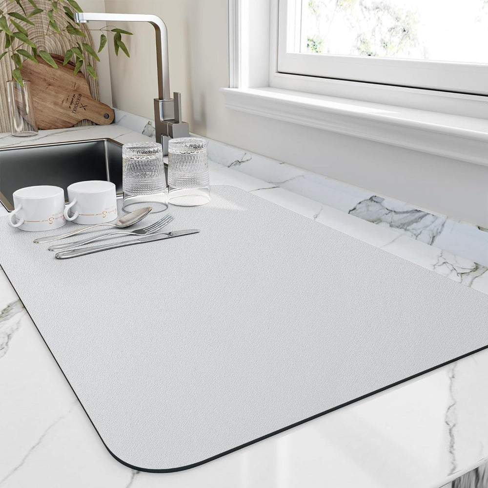White diatomite quick-dry dish mat on a marble countertop with cups, glasses, and cutlery.