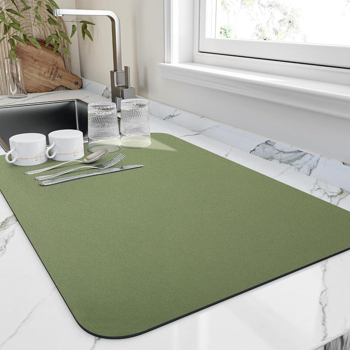 Green diatomite quick-dry dish mat on a marble countertop with cups and cutlery.