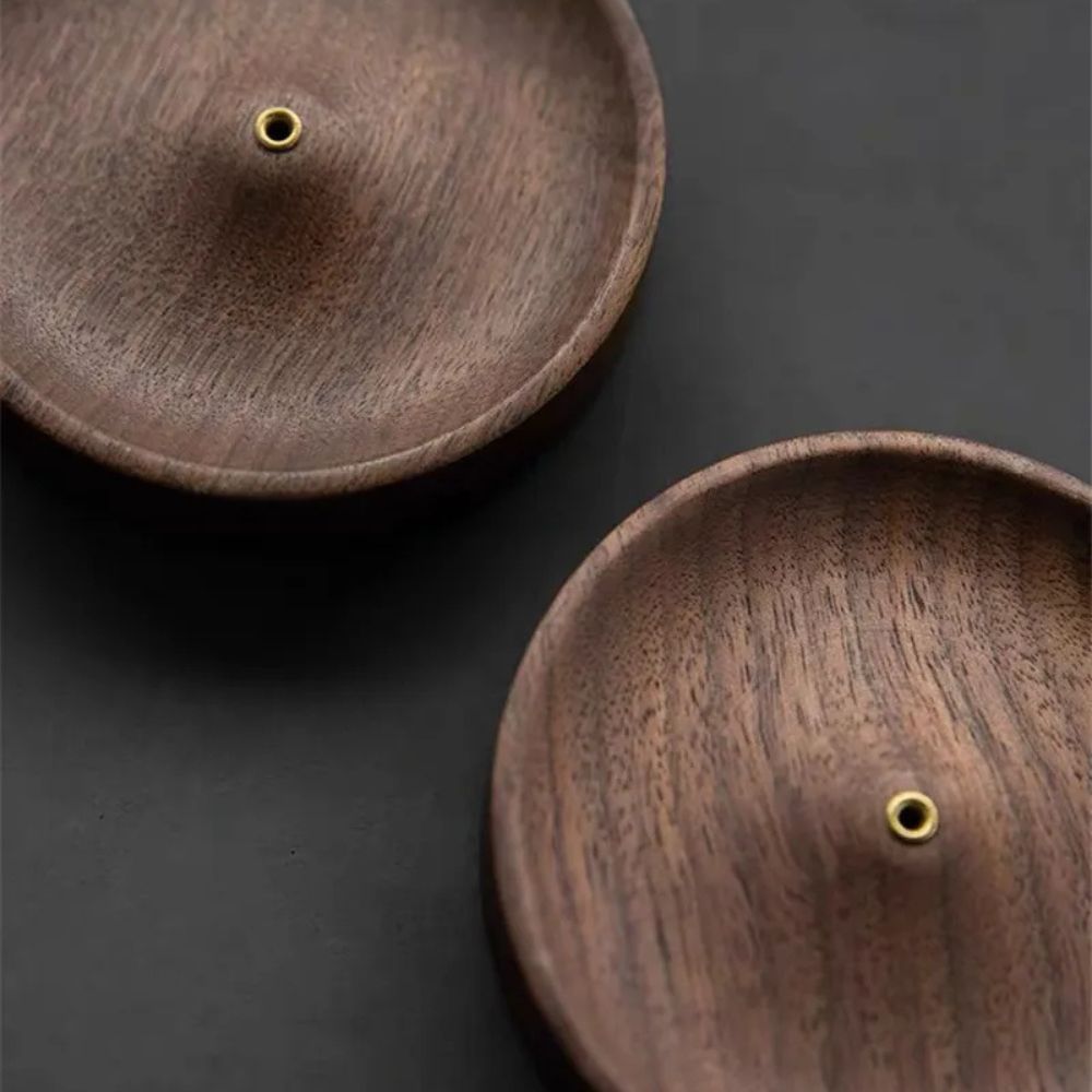 Two round, natural wood incense holders with a brass hole in the center of each.