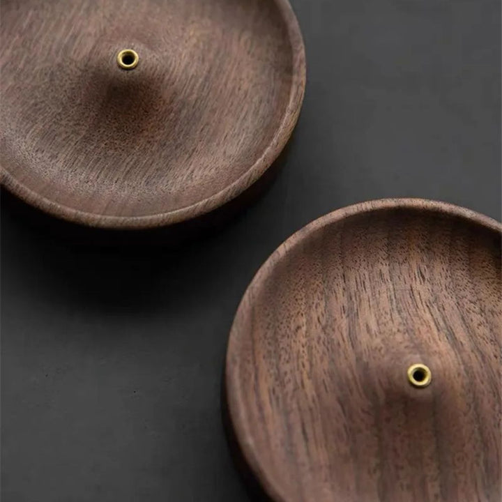 Two round, natural wood incense holders with a brass hole in the center of each.