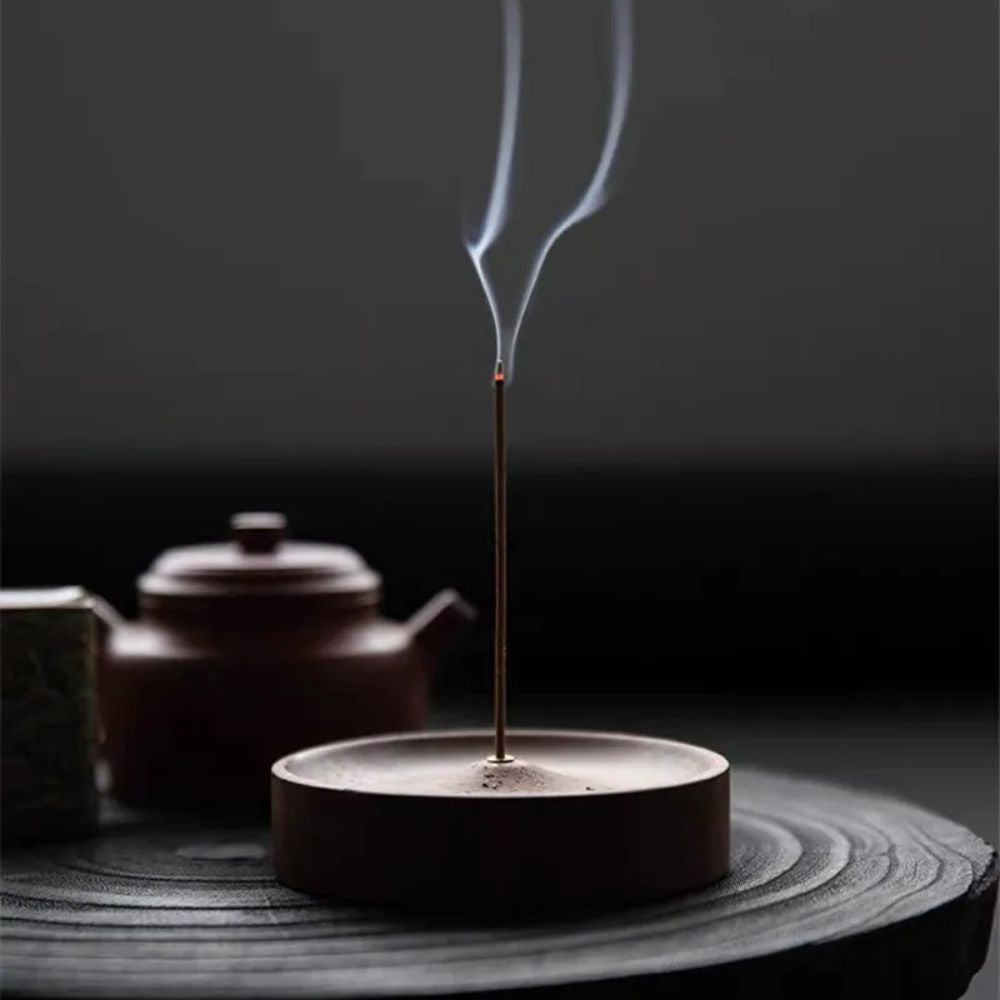Round wood incense holder with an incense stick burning and smoke rising.