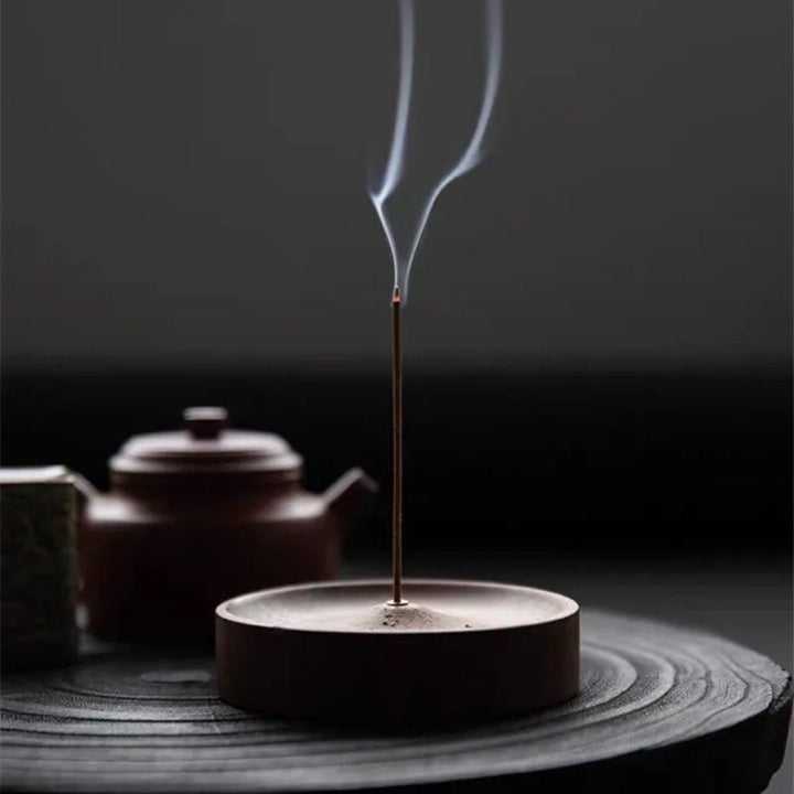 Round wood incense holder with an incense stick burning and smoke rising.