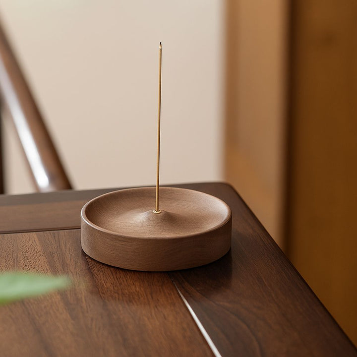 Round wooden incense holder with a single incense stick burning in the center.