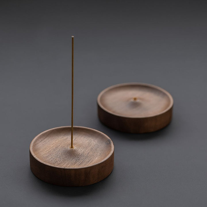 Round wood incense holder with an incense stick in the center, another holder in the background.