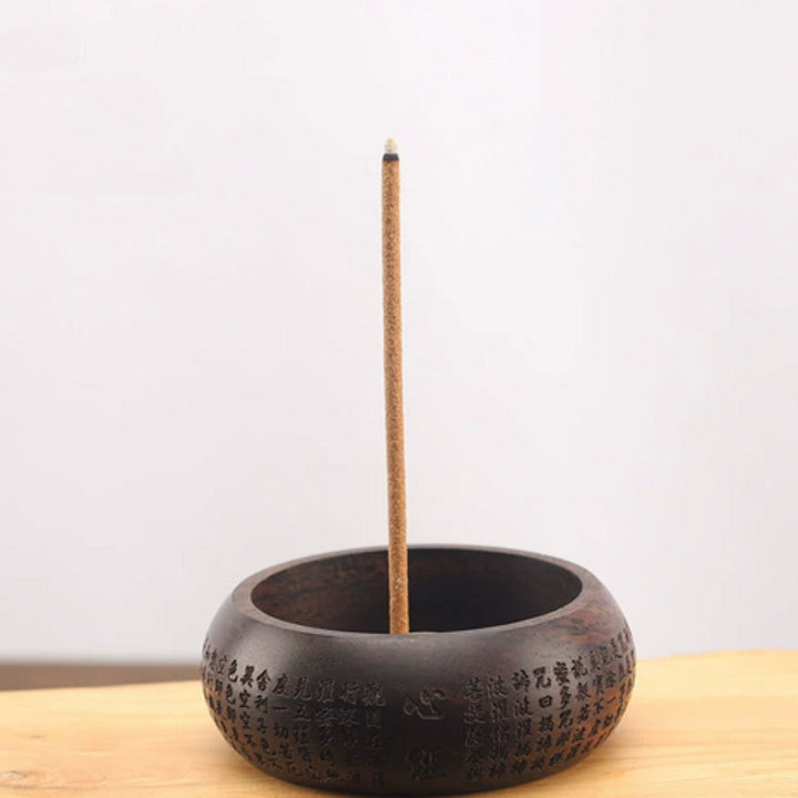 Solid wood incense holder with a single incense stick burning.