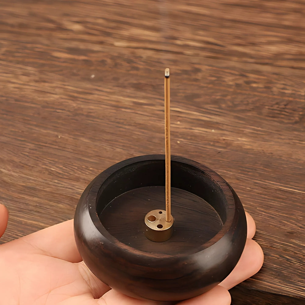 Solid wood incense holder with a brass insert holding a lit incense stick.