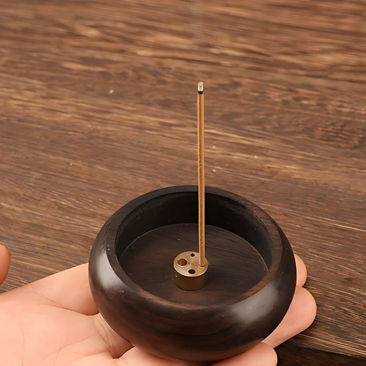 Solid wood incense holder with a brass insert holding a lit incense stick.