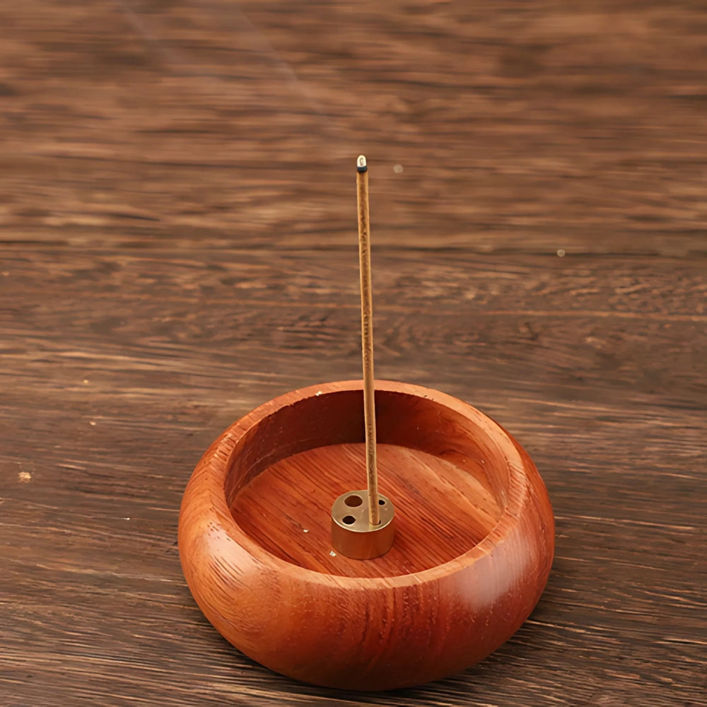 Solid wood incense holder with a brass insert holding a lit incense stick.
