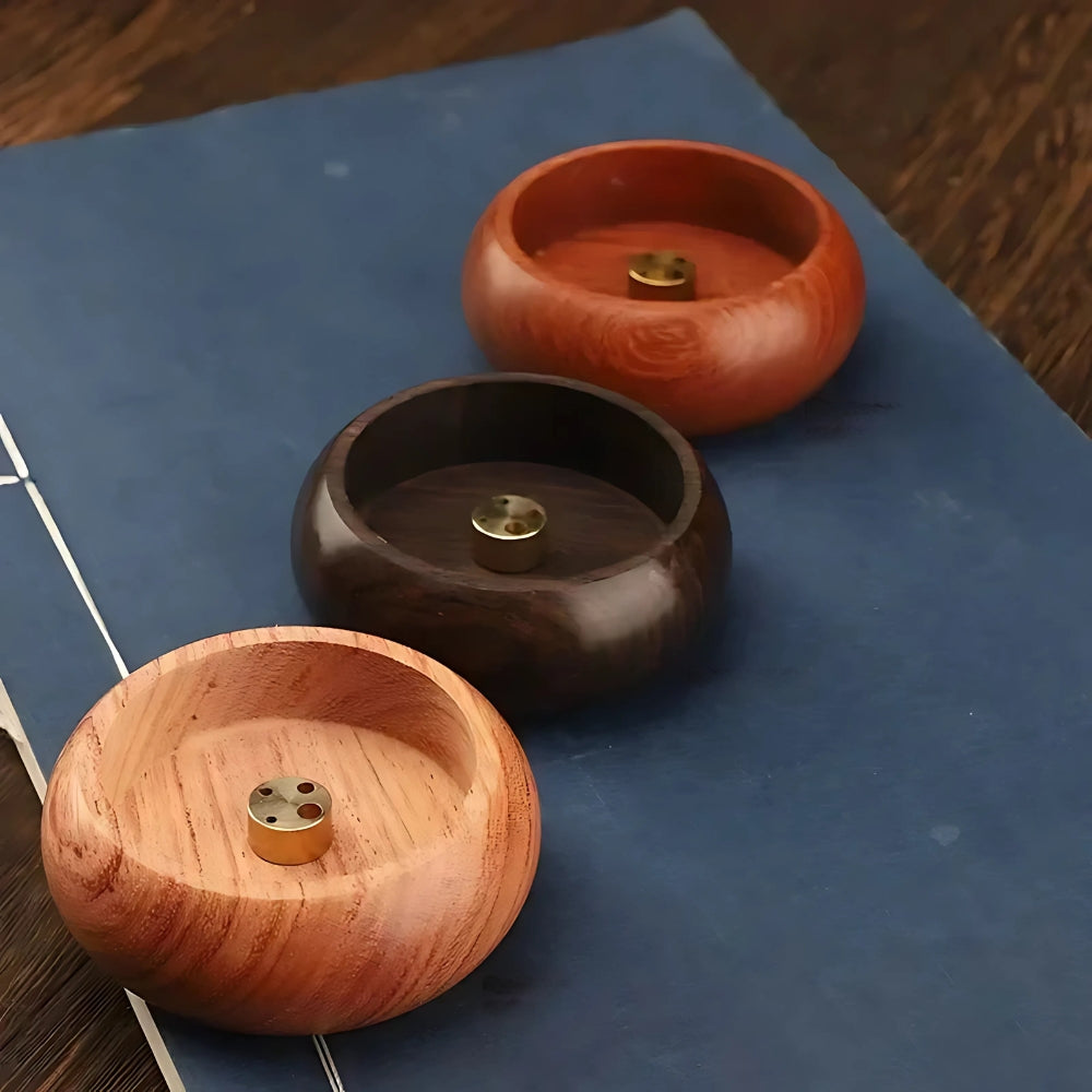 Three round solid wood incense holders with brass inserts, arranged on a blue surface.