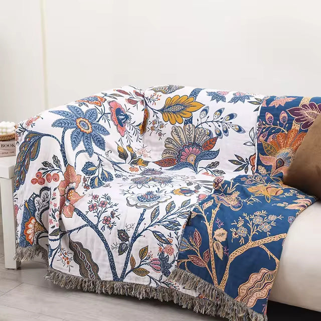 Reversible floral cotton throw blanket draped over a sofa, featuring a white base with blue, pink, and yellow floral patterns.