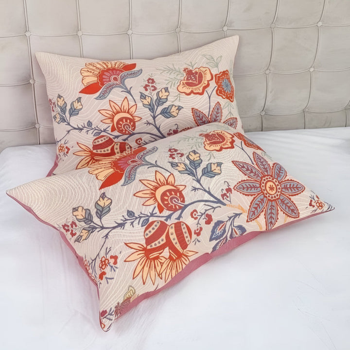 Two rustic floral boho pillowcases in beige with red and blue floral patterns on a bed.