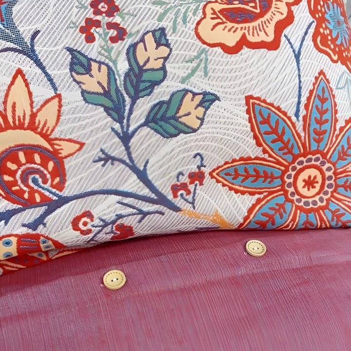 Close-up of a rustic floral boho pillowcase with blue and red flowers on a textured white background, next to a pink surface with two buttons.