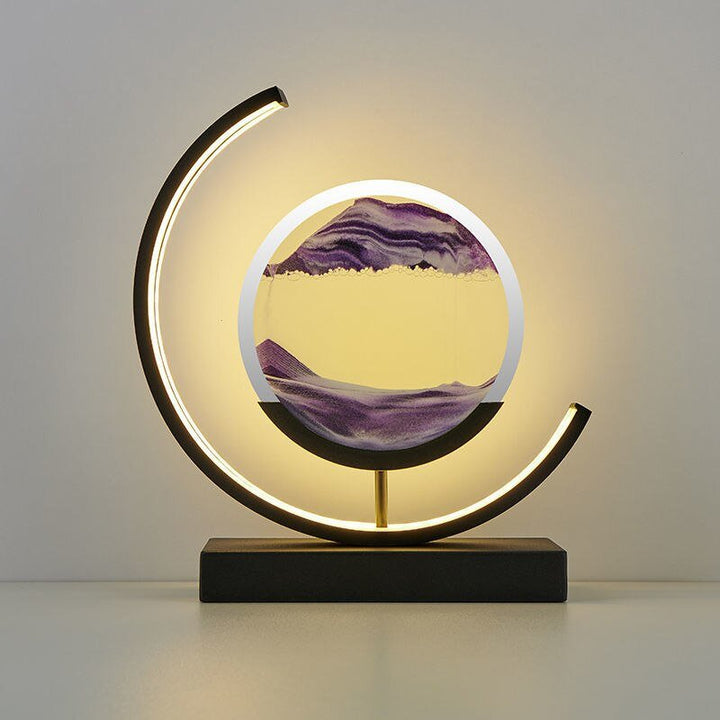 Modern black lamp with a crescent shape and a circular glass enclosure containing flowing purple sand.