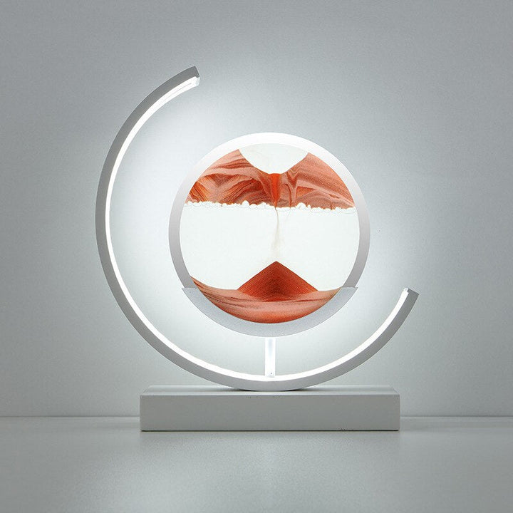 Modern white lamp with a circular glass enclosure containing flowing red and white sand, illuminated by a curved LED light.