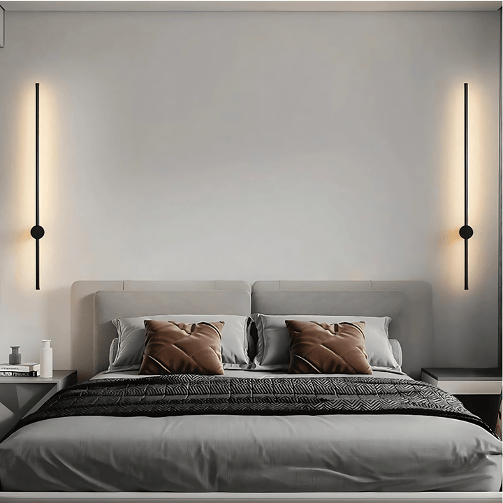 Black satin wall sconce with a sleek, modern design, illuminating a bedroom wall.