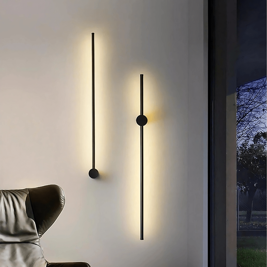 Two black satin wall sconces with a modern, sleek design, one longer than the other, casting a warm glow on a white wall.