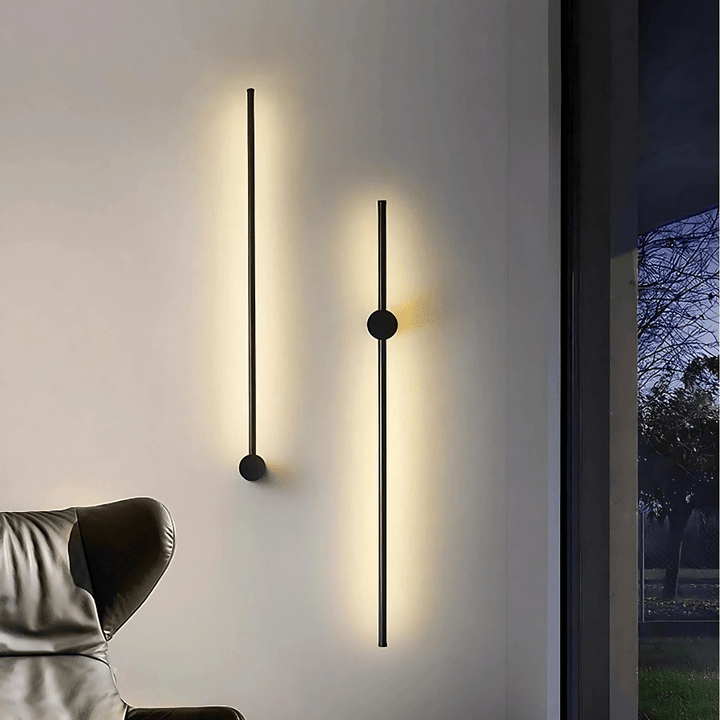 Two black satin wall sconces with a modern, sleek design, one longer than the other, casting a warm glow on a white wall.