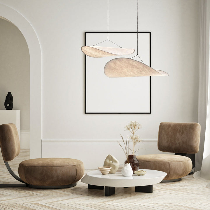 Two minimalist pendant lights resembling sails hang above a coffee table in a modern living room.