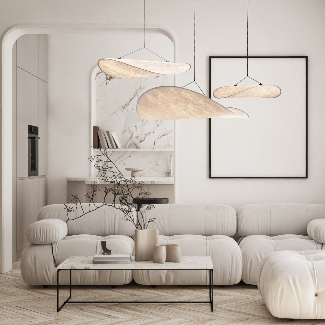 Three minimalist pendant lights with a sail shape hang above a modern sofa and coffee table.