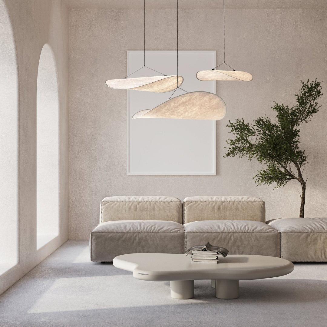 Three minimalist pendant lights resembling sails hang above a sofa and coffee table in a modern living room.