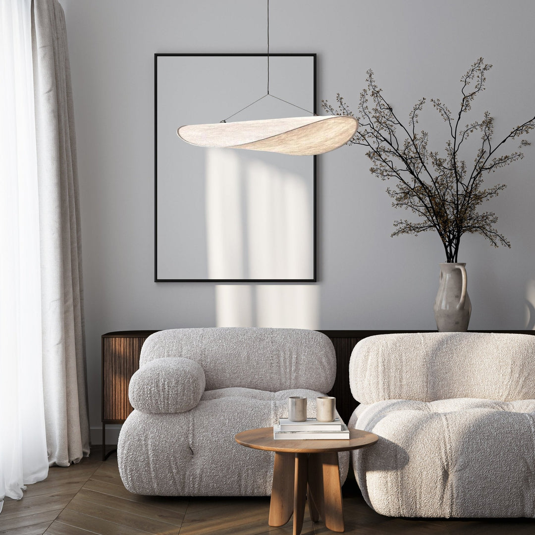 Minimalist pendant light with a sail shape, suspended above a living room setting.