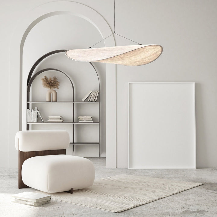 Minimalist pendant light resembling a sail, hanging over a chair and rug.