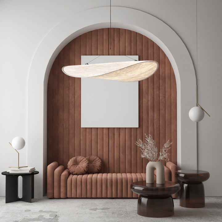 Modern minimalist pendant light with a sail-like shape, illuminating a living space with a sofa and side tables.