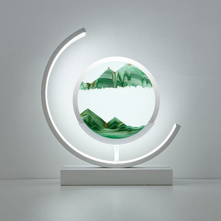 White curved lamp with a circular glass enclosure containing flowing green sand art.