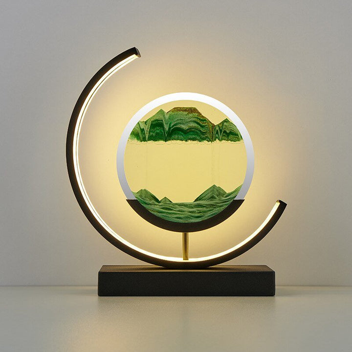 Modern desk lamp with a circular frame containing moving sand art and a crescent LED light.