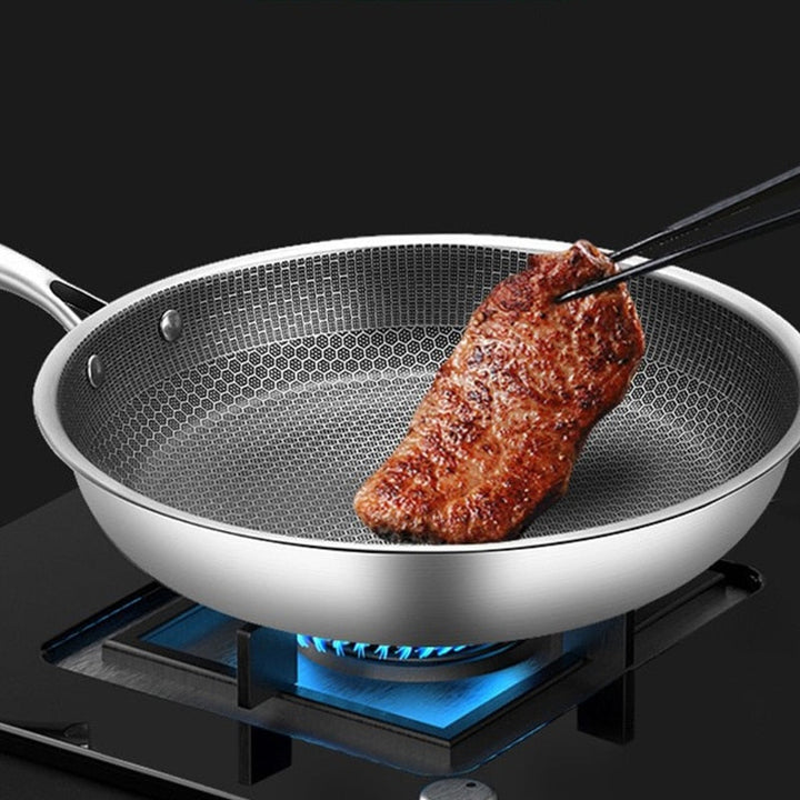 Honeycomb stainless steel frying pan with a steak being cooked on a gas stove.