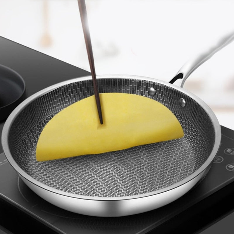 Honeycomb stainless steel frying pan with a yellow omelette being folded with chopsticks.