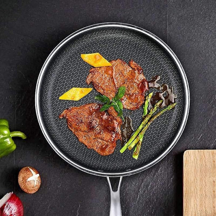 Honeycomb stainless steel frying pan with two steaks, asparagus, and mango slices.
