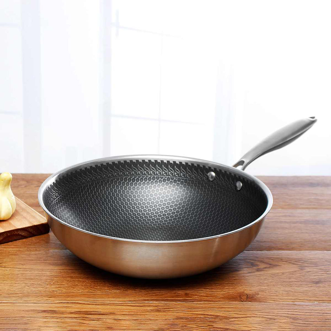 Honeycomb stainless steel frying pan with a silver handle on a wooden table.