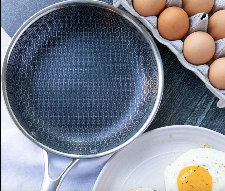 Honeycomb stainless steel frying pan with a fried egg on a plate and a carton of eggs.
