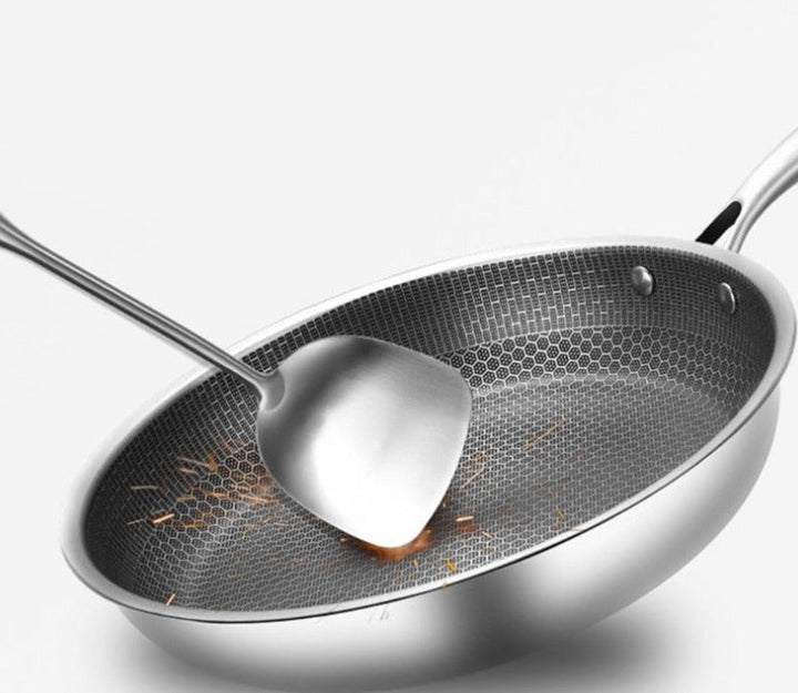 Stainless steel frying pan with honeycomb pattern and a metal spatula, showing sparks.
