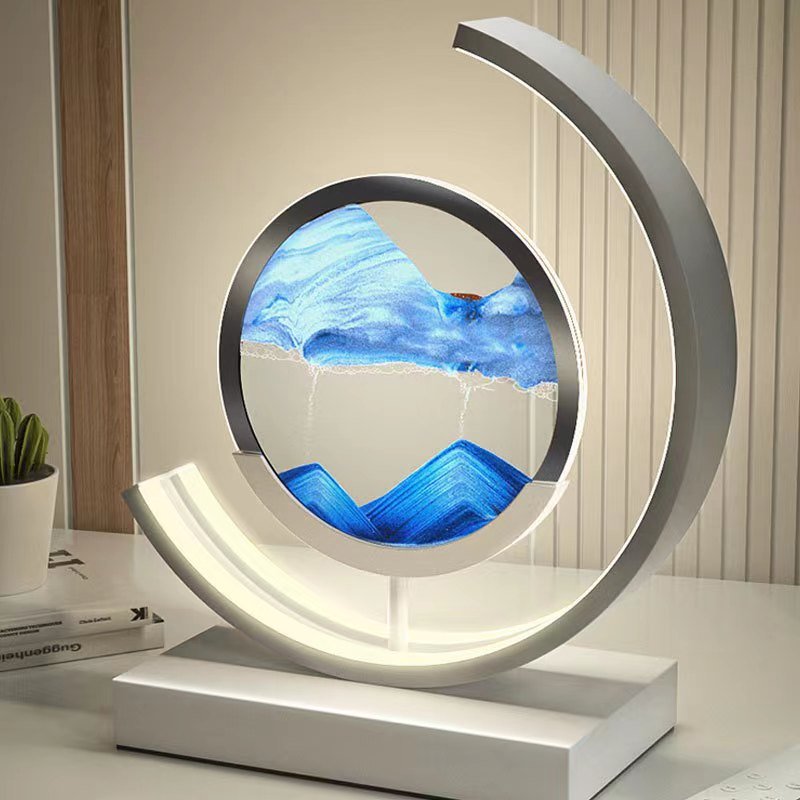 Quicksand LED table lamp with blue sand art and a modern curved metal frame.
