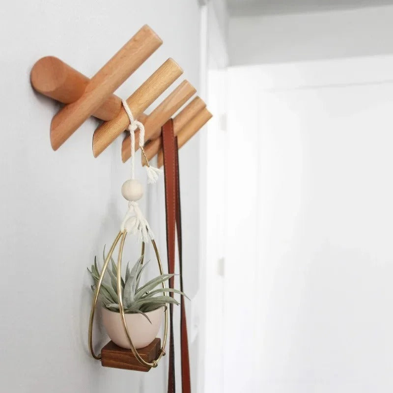 Solid oak wall coat rack with four pegs, holding a brown leather belt and a hanging plant.