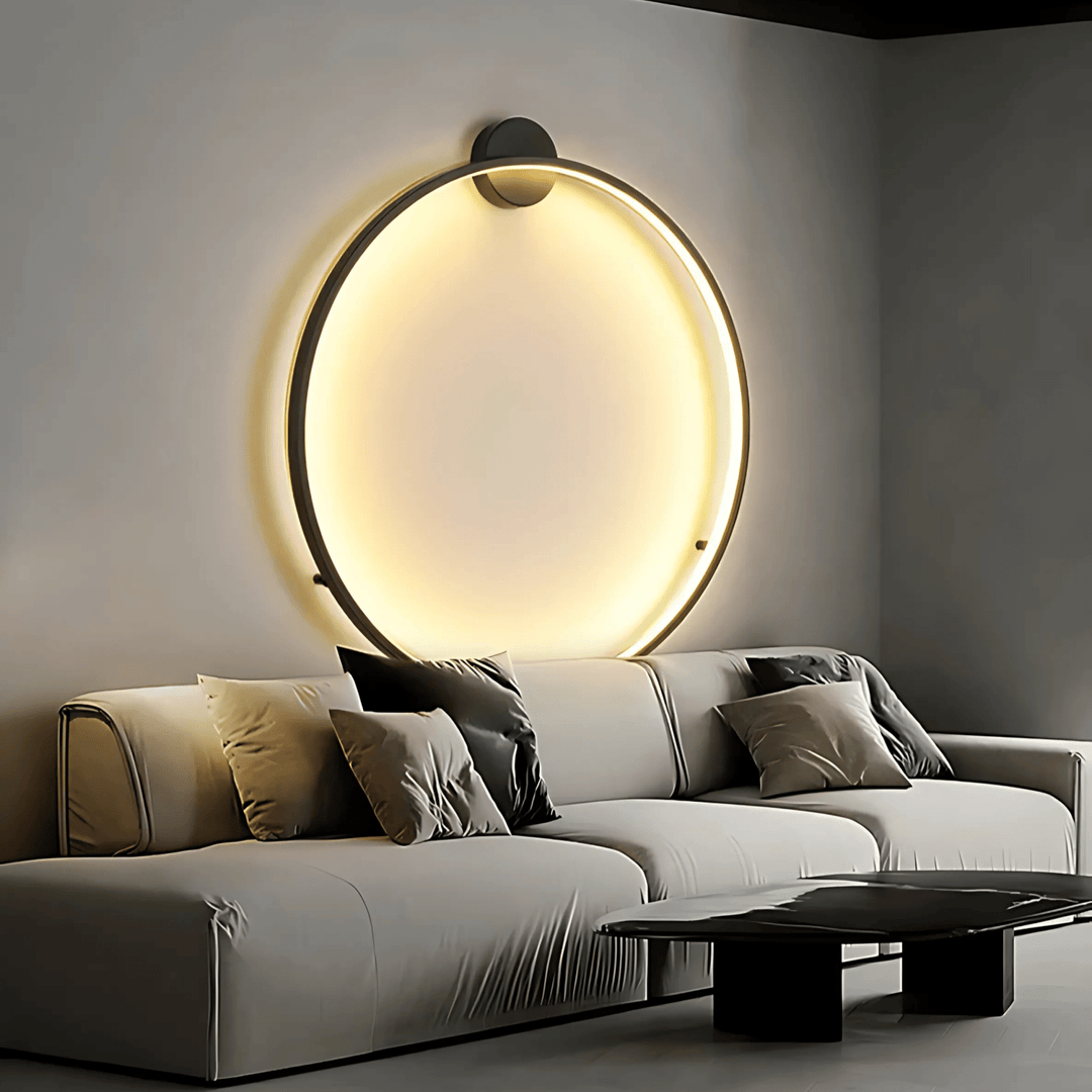Modern circular wall sconce with warm ambient lighting above a light gray sectional sofa.