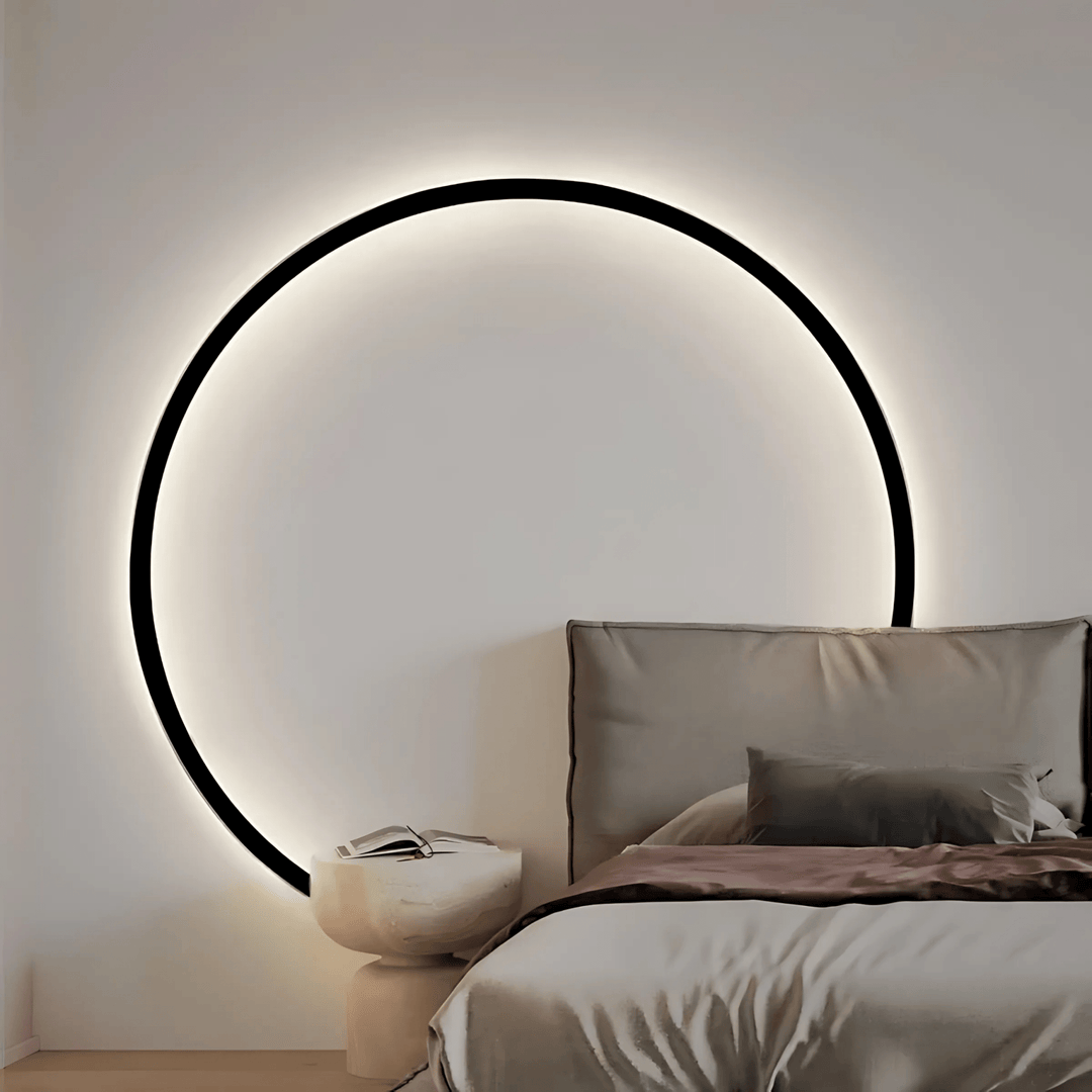 Modern circular wall sconce with black frame and soft ambient light, above a bedside table and bed.
