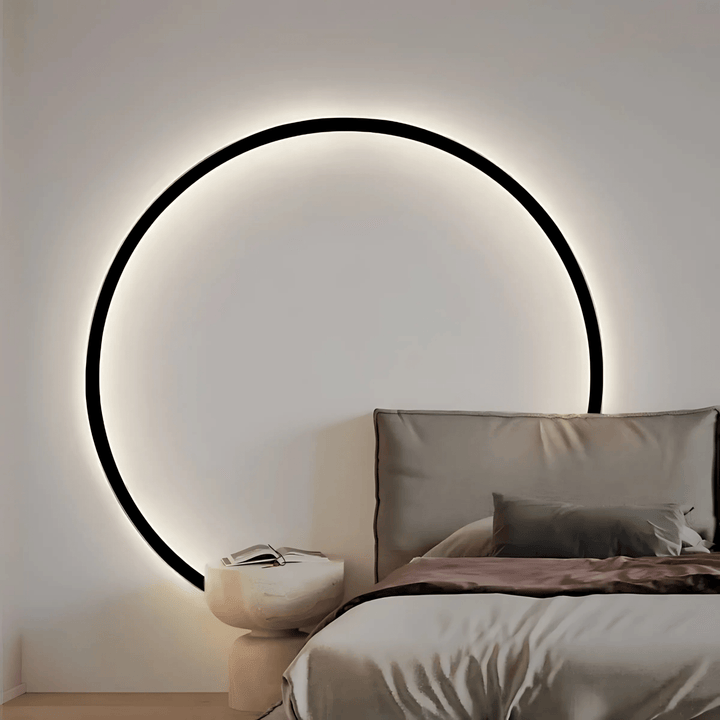Modern circular wall sconce with black frame and soft ambient light, above a bedside table and bed.