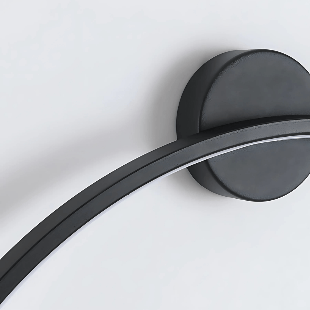 Black modern wall sconce with a curved arm and a circular base against a white background.