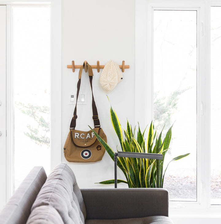 Beechwood wall coat rack with 5 hooks, holding a brown bag and a cream-colored hat.
